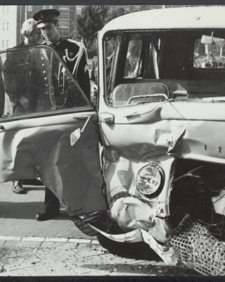 Foto van een kapotte auto en de Koninklijke Marechaussee.