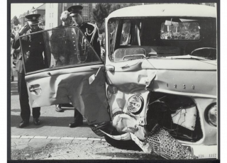 Foto van een kapotte auto en de Koninklijke Marechaussee.
