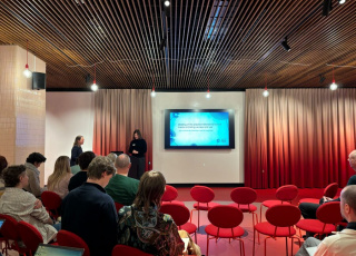 Afbeelding van een zaal met spreker en aanwezigen.